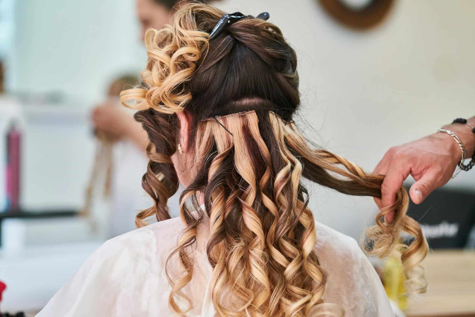 A woman with long, curly hair is having her balayage styled at Sofoklis Hair Salon.